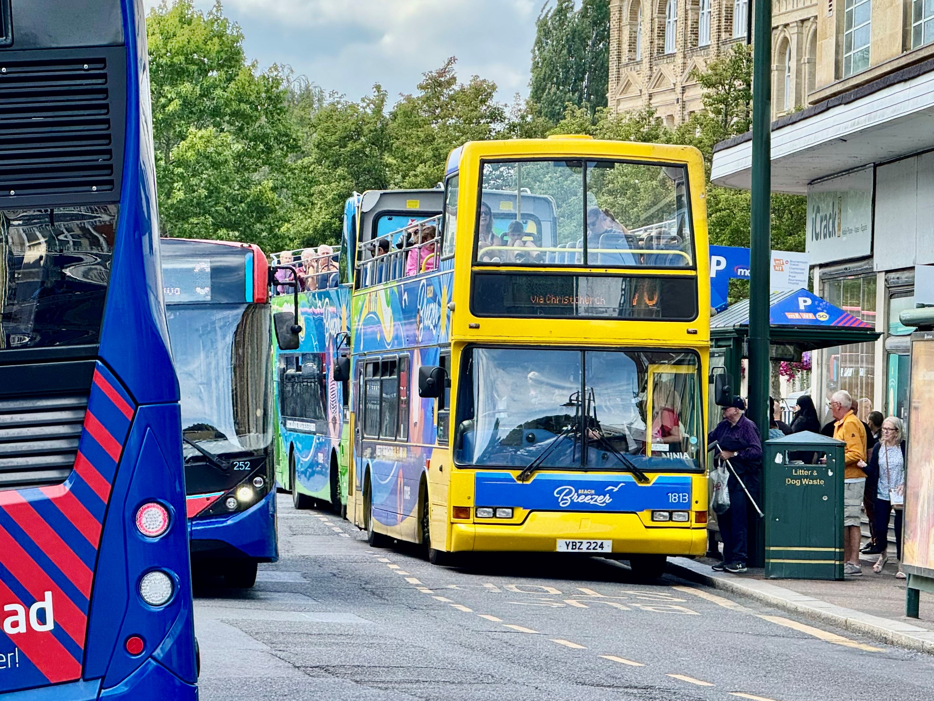 A yellow open-top breezer bus is at a bus stop in Gervis Place with people getting on it