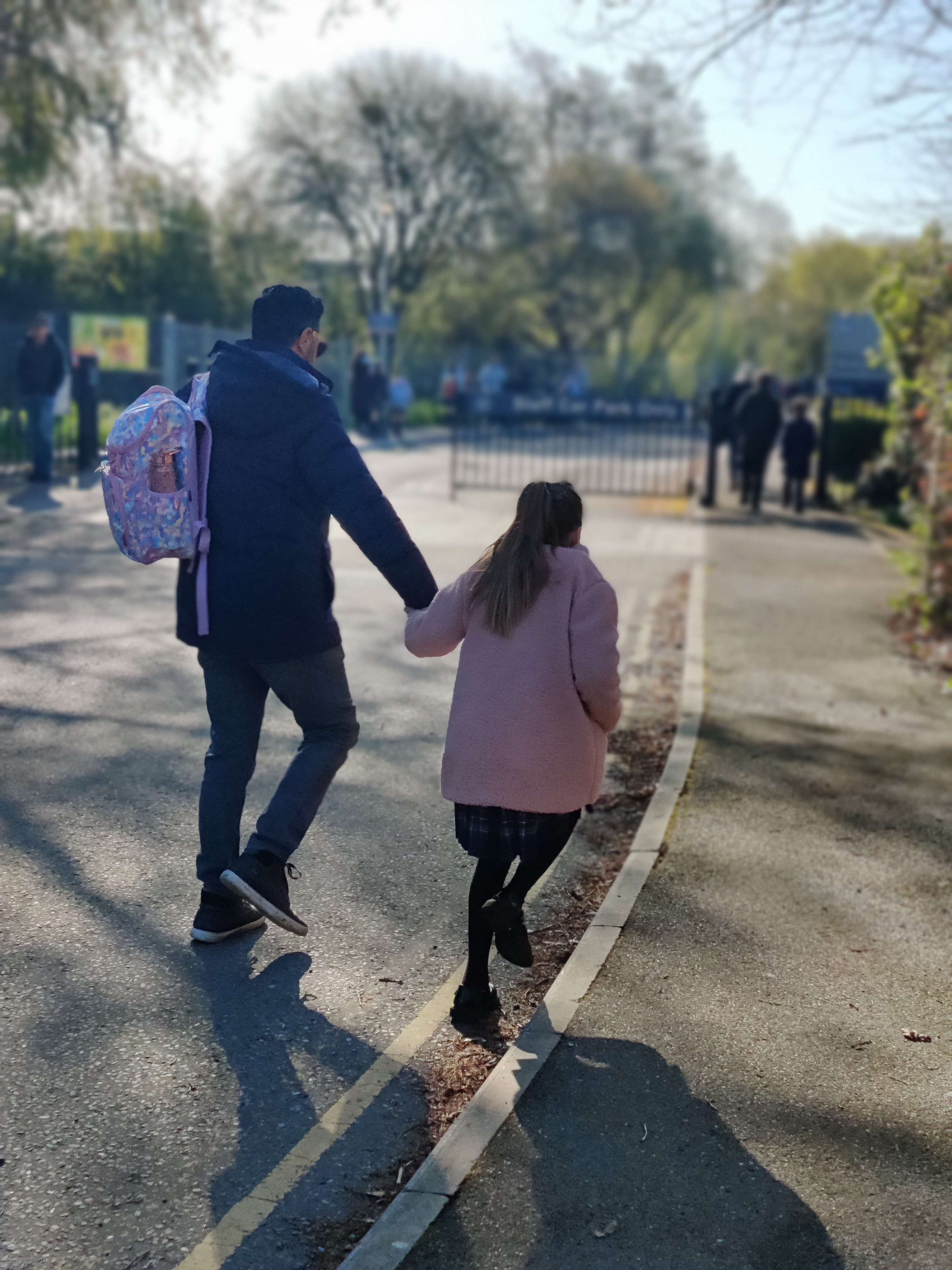 A father and daughter holding hands and walking to approach the school gate.