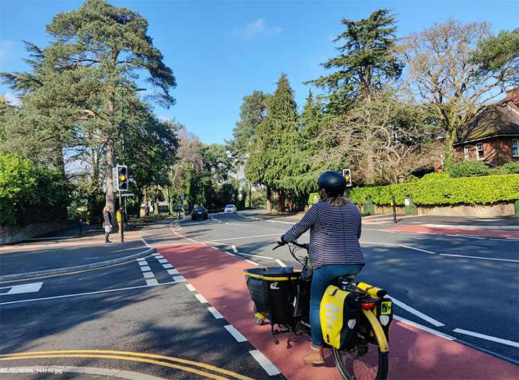 A woman on a cargo bike approaching an amber light at a toucan crossing