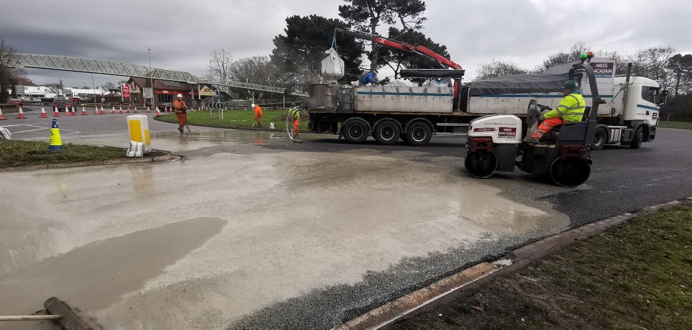 Asphalt covering a road, being overseen by construction workers